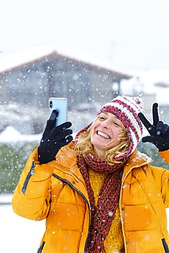 Caucasian young woman enjoying with a mobile phone in snow outdoor in winter time. Navarre, Spain, Europe.