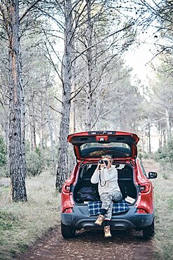 Young adult caucasian woman taking pictures close to a car parked in a forestry path in autumn. Travels concept. Ayegui, Navarre, Spain, Europe.