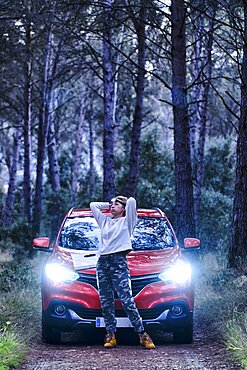 Car and young adult caucasian woman lost in wooded area trying to orient herself at dusk. Travels concept. Ayegui, Navarre, Spain, Europe.