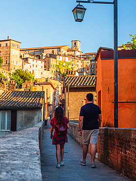 A couple walking in Perugia's Aqueduct street with the cityscape in the back at sunset, Perugia, Umbria, Italy, Europe