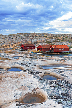 Red traditional wooden cottages on granite rock in a cloudy day, Ramsvik island, Bohuslan, Vastra Gotaland, Sweden, Scandinavia, Europe