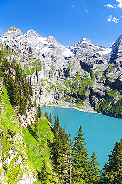 Elevated view of the crystal blue water of the lake of Oeschinensee among pine trees and alpine peaks covered with snow, Oeschinensee, Kandersteg, Bern Canton, Switzerland, Europe