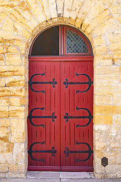 Saintes-Maries-de-la-Mer, Bouches-du-Rhone, Provence-Alpes-Cote d'Azur, France. Red door with metal hinges in a stone building.