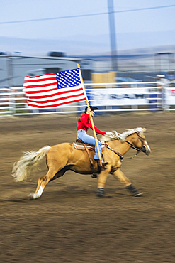 USA, Washington State, Whitman County. Palouse. Palouse Empire State Fair. Colfax. September 9, 2021. Woman riding with American flag at a rodeo.