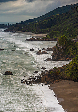 Curving Shoreline with Offshore Rocks and Bush-Covered Cliffs Under Moody Skies, Punakaiki Coast, West Coast, New Zealand