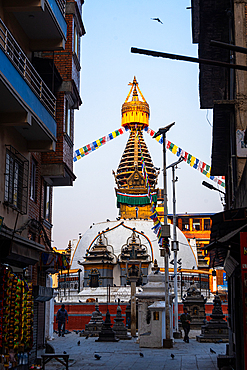 Vertical street-level view of Kathi Swoyambhu Shree Gha Stupa framed by narrow alley walls and dense prayer flags