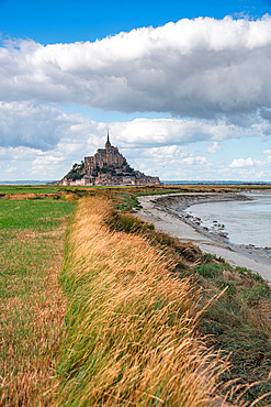 Long path through windswept grass leading towards Mont Saint-Michel, the famous tidal island abbey, Normandy, France.