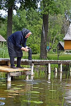 Old woman washing clothes in front of her house by the Baluosykstis lake around Ginuciai, Aukstaitija National Park, Lithuania, Europe