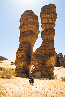 Man squatting beside the extraordinary sandstone rock structure called 'Dancing Rocks' in the Sharaan Nature Reserve, AlUla, Medina Province, Saudi Arabia, Middle East