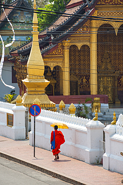 Novice monk walking in Sakkarine Rd in front of Wat Sop temple, Luang Prabang, northern Laos, Southeast Asia