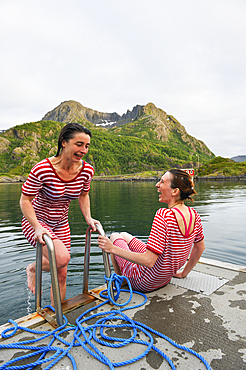 Young women , dressed with an old-fashioned swimming costume, bathing into the icy water of the fjord.Hamn i Senja Hotel.Senja island.County of Troms,Norway,Northern Europe