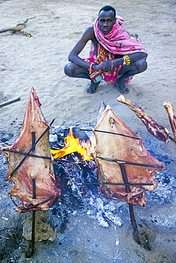 Slow cooking of meat around a campfire in the bush, in Namanga region, Kenya, East Africa