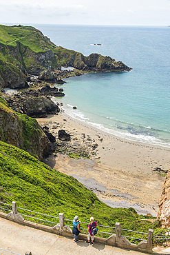 Two women looking at the Grande Greve Bay from La Coupée, the narrow isthmus which links Greater and Little Sark, Sark island, Channel Islands, Bailiwick of Guernsey, United Kingdom