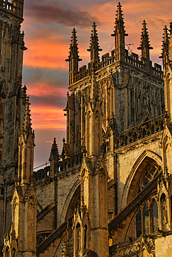 A close-up view of a stone cathedral against a sunset sky. The image focuses on the intricate details of the gothic architecture, including pointed arches, spires, and gargoyles in York, North Yorkshire, UK.