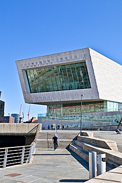 Museum of Liverpool with an angled facade, large glass windows, clear blue sky, and a man walking up the steps toward the entrance.