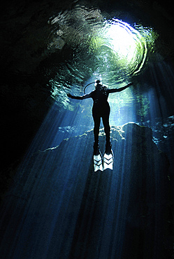 A cavern diver ascends into the light filtering into cenote system at Yucatan Peninsula, Mexico.
