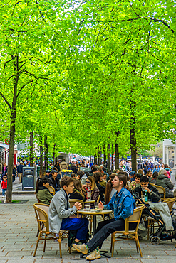 Diners on restaurant terrace under new leaves on Rue Saint-Martin on spring day