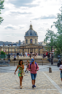 Tourists crossing Pont des Arts bridge, the Acadamie Francaise in the background, day, in summer