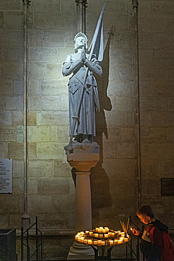 Boy lighting candle below statue of Joan of Arc in Notre Dame cathedral