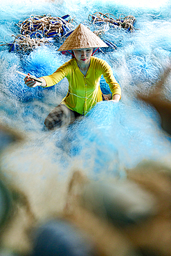 Women in a traditional ao dai mending a fishing net, Vietnam