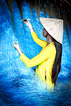 Women in a traditional ao dai mending a fishing net, Vietnam