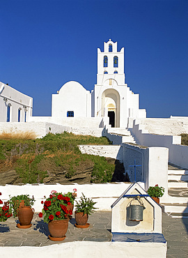 Pots of geraniums beside a well in front of the white walls and bell tower of the Monastery of Panagia Chrysopigi on Sifnos, Cyclades, Greek Islands, Greece, Europe