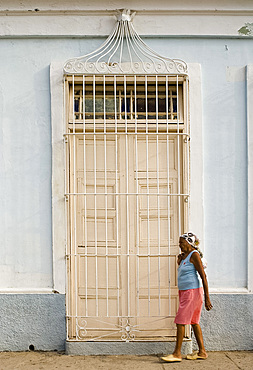 A woman walking past a typical door with ornate iron bars, Trinidad, Cuba, West Indies, Central America