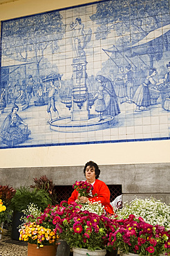 A woman selling flowers outside the main market, in front of a mural made from old Portuguese blue and white tiles, Funchal, Madeira, Portugal, Europe