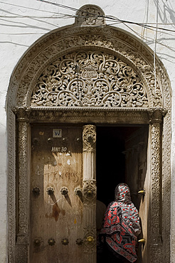 Woman wearing colourful headscarf going through a carved wooden Arab door in Stone Town, Zanzibar, Tanzania, East Africa