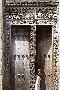 Young boy looking out of an intricately carved wooden Arab door in Stone Town, Zanzibar, Tanzania, East Africa