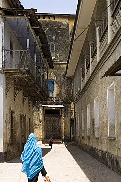 A woman in a colourful headscarf walking down a narrow street in Stone Town, Zanzibar, Tanzania, East Africa, Africa