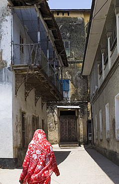 A woman in a colourful headscarf walking down a narrow street in Stone Town, Zanzibar, Tanzania, East Africa, Africa