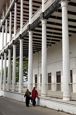 Two women in Islamic dress walking past the pillars on the House of Wonders, Stone Town, UNESCO World Heritage Site, Zanzibar, Tanzania, East Africa, Africa