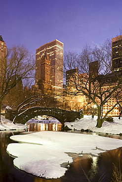 A view of the Gapstow Bridge in Central Park and city skyline at dusk after a snow storm, New York City, New York State, USA