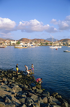 Boys on the rocks, with the harbour and town in the background, at Mindelo, Sao Vicente Island, Cape Verde Islands, Atlantic, Africa