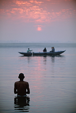 Boat passing a man standing in the holy river , River Ganges (Ganga), Varanasi (Benares), Uttar Pradesh state, India, Asia