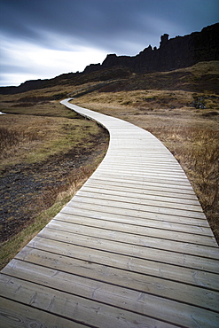 Boardwalk meandering towards rugged cliffs and stormy sky at Thingvellir National Park near Reykjavik, Iceland, Polar Regions