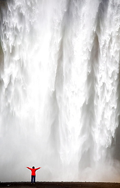 Woman in red jacket standing in front of Skogafoss waterfall, South Iceland, Iceland, Polar Regions