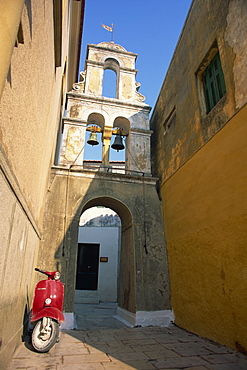 Red scooter parked beneath a bell tower in a back street of Gaios Town on Paxos, Ionian Islands, Greek Islands, Greece