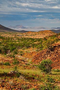 Colourful rocky landscape high up in the hills, with mountain camp in the background, Etendeka, Namibia, Africa