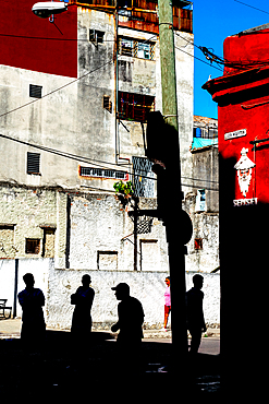 Silhouetted figures against brightly coloured buildings, basketball net on street corner, San Martin, Old Havana, Cuba