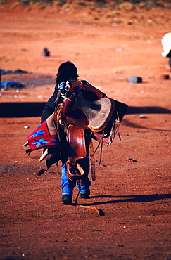 Usa, Az, Kayenta, Navajo Child Walking With His Saddle