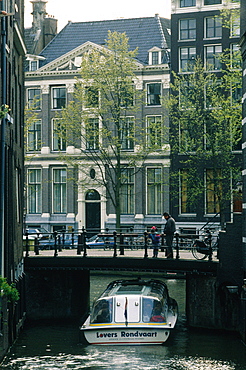 Netherlands, Amsterdam, Tour Boat Passing Under A Narrow Bridge On A Canal