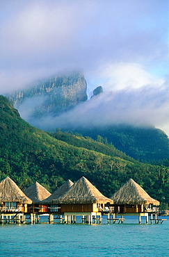 French Polynesia, The Leeward Islands (Iles Sous-Le-Vent), Bora-Bora Island, View Of Hotel Huts Built On The Lagoon, Mist On The Otemanu Mountain At Back