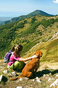 Girl and dog, looking at view of Camaiore and Tyrrhenian Sea from Apuan Alps (Alpi Apuane), Lucca Province, Tuscany, Italy, Europe