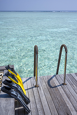 Fins (flippers) drying on a deck overlooking the crystal clear lagoon on an exotic Island in the Maldives. Indian Ocean.