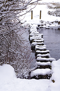 Stepping stones over the River Rothay in winter snow at Rydal Water in the Lake District National Park.