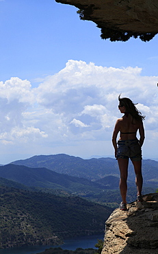 A woman looks out across the hills of Catalonia from a rock ledge near the village of Siuarana, near Reus and Barcelona, Catalonia, Spain, Europe