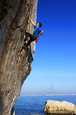 A climber tackles a difficult route on the limestone sea cliffs of Akyalar, with the city of Antayla in the distance, Anatolia, Turkey, Asia Minor, Eurasia