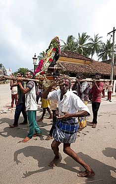 Men dancing to drumbeat as bronze deity covered with puja mala (garlands) being carried along the street, Tranquebar, Tamil Nadu, India, Asia